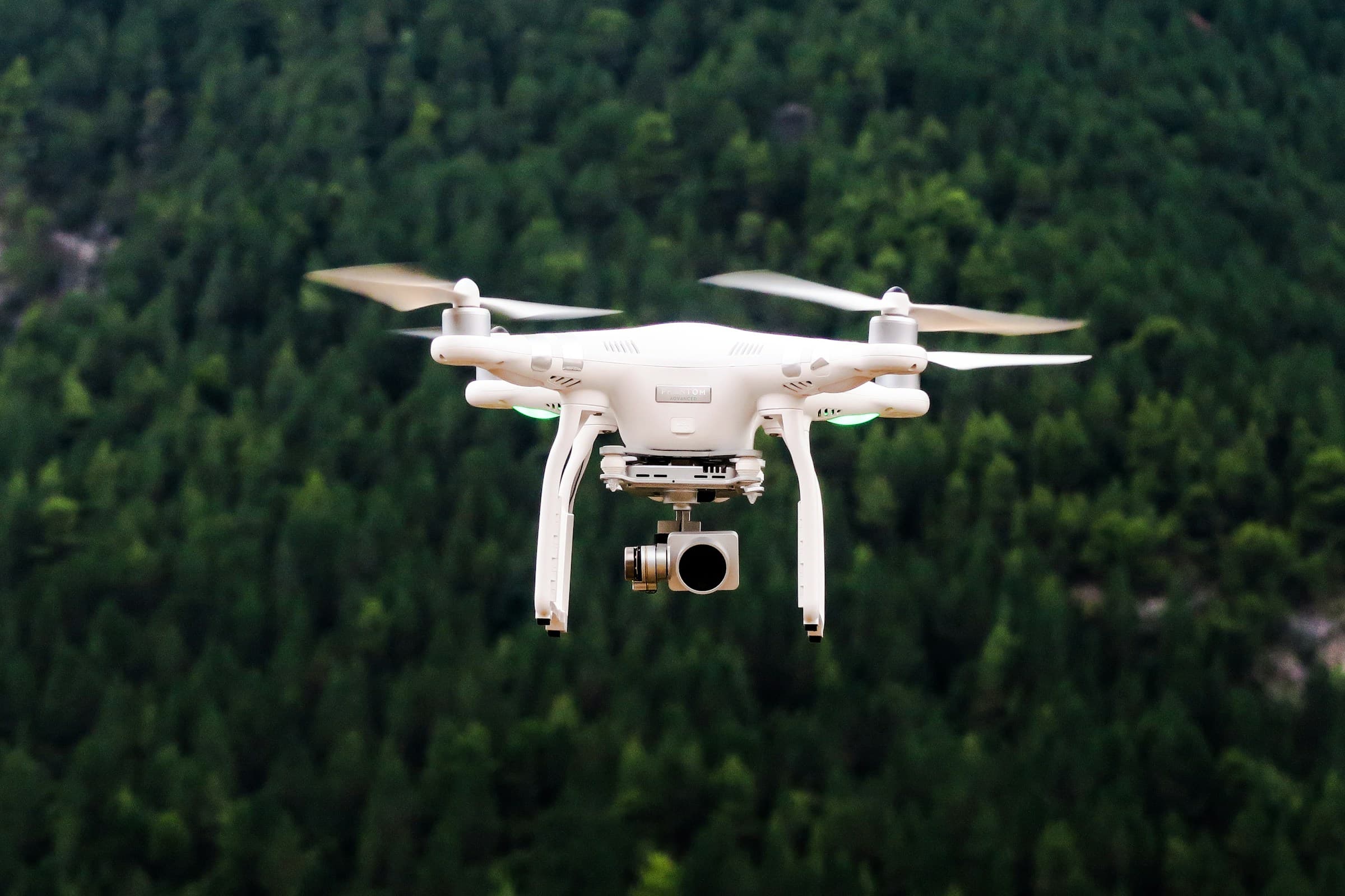 A white quadcopter hovering in front of a forest — illustrative aircraft photography